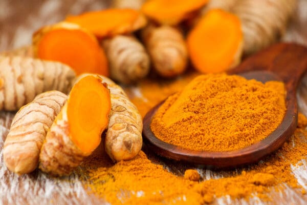 A wooden bowl of turmeric next to some ginger.