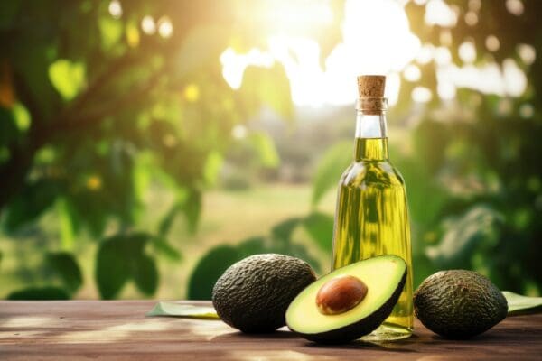 A bottle of oil and two avocados on a table.