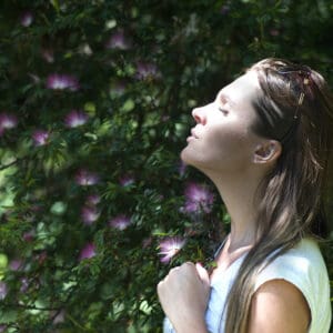 A woman with her eyes closed in front of some bushes