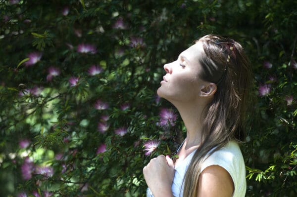 A woman with her eyes closed in front of some bushes