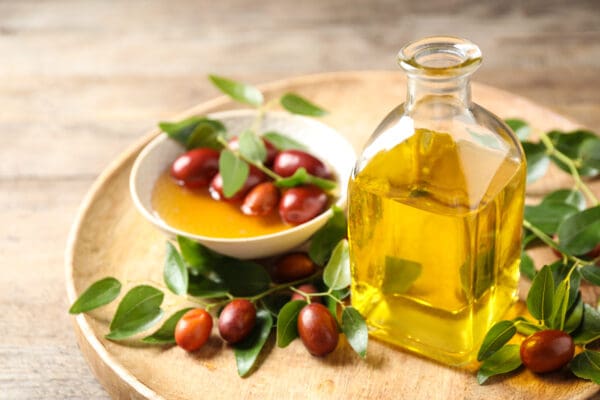 A bowl of fruit and a bottle of oil on a wooden table.