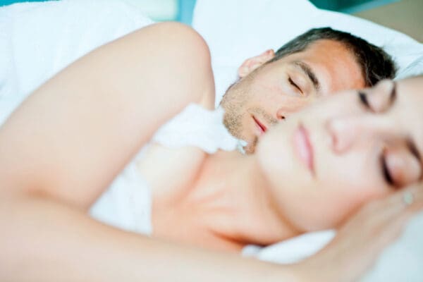 A man and woman sleeping in bed with one of them laying on the floor.