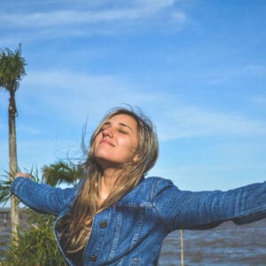 A woman in blue jacket standing near body of water.