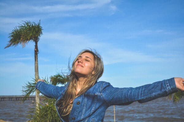 A woman in blue jacket standing near body of water.