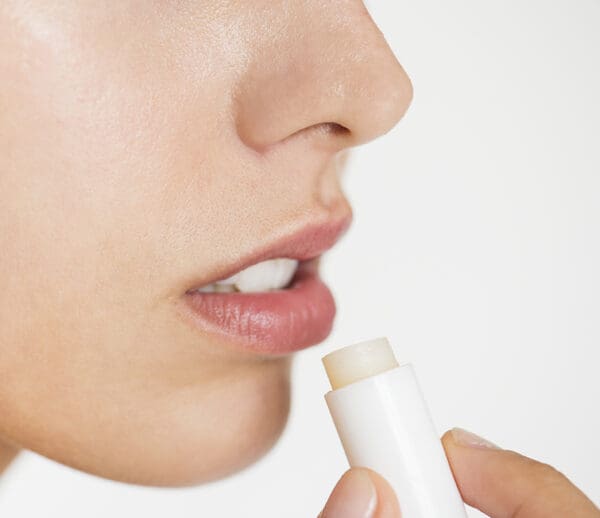 A woman is putting lip balm on her lips.