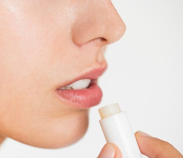 A woman is putting some lip balm on her lips.