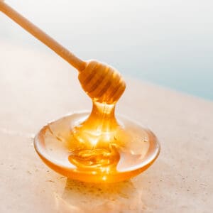 A honey stick is being held over a bowl of honey.