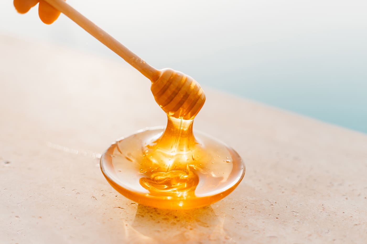 A honey stick is being held over a bowl of honey.